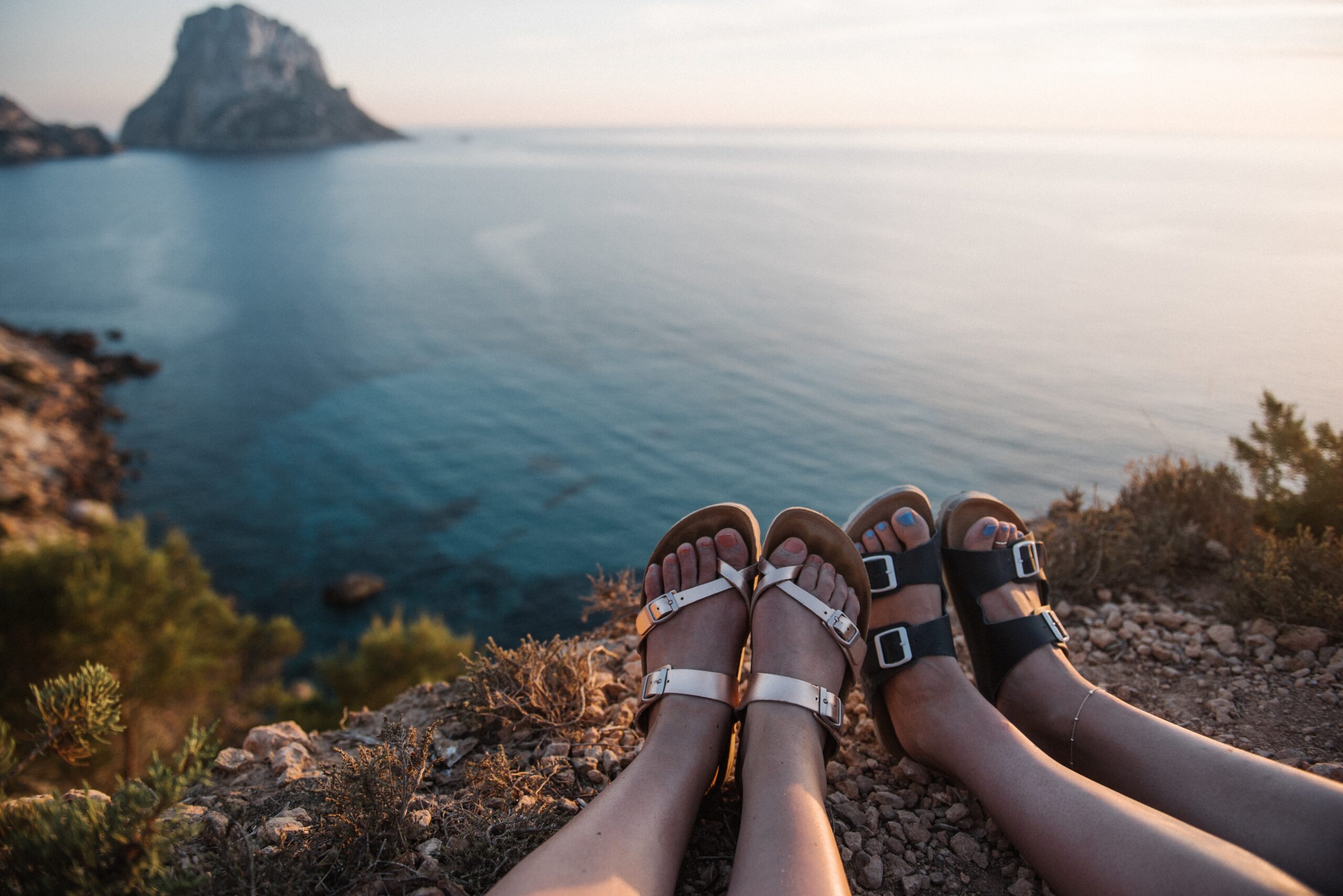 females sitting on a cliff by the sea enjoying the beautiful view of the sunset