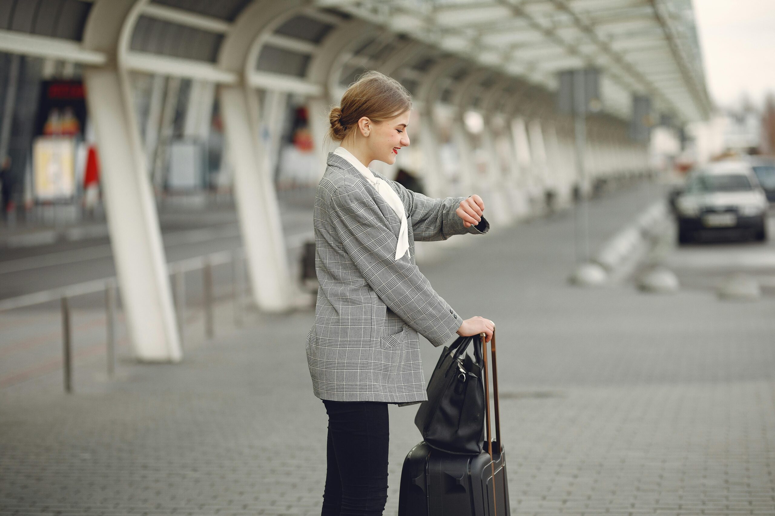 Woman in gray jacket checking wristwatch at station with luggage, representing punctual travel.